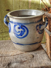 Load image into Gallery viewer, Grey and blue Betschdorf confit pot sitting on a low, weathered rustic farmhouse stool. In the background is a rustic farmhouse door painted in sage green, with sunlight streaming in from the left.