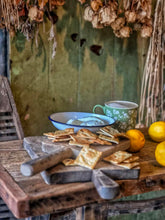 Load image into Gallery viewer, Antique Hungarian oak chopping board with a distinctive tulip-shaped outline and long handle, displayed with cheese and rustic food on a weathered wooden table. The solid oak board has a few historic cutting scars and natural aged wood texture. The board measures 13 inches (33 cm) long including the handle, resting on a weathered wood plank background.