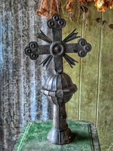 Load image into Gallery viewer, An ornate dark metal Orthodox cross with a ribbed central stem and decorative crossbar, displayed on a green surface against a rustic corrugated metal and wood wall backdrop.