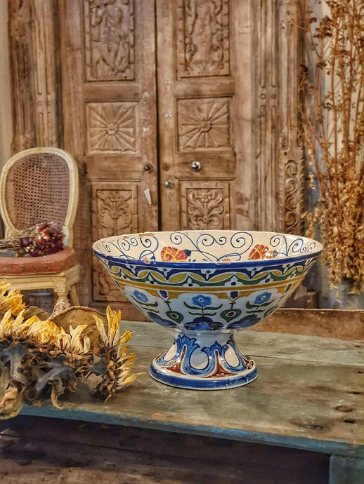 Antique Italian Deruta majolica bowl (yellow, blue, green) sitting on a rustic duck egg blue chopping board next to a bunch of dried sunflowers. The display is set on a weathered French workbench against a large, bleached-out Indian door.
