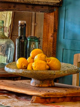 Load image into Gallery viewer, A heavy, hand-formed Moroccan Tamegroute footed serving dish with a soft cream ground and a delicate green splatter glaze. The shallow pedestal bowl features a rough, textured, salt-fired crystalline finish and is styled filled with bright lemons against a backdrop of weathered timber and rustic country-house furniture.