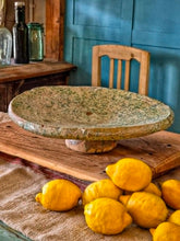 Load image into Gallery viewer, A heavy, hand-formed Moroccan Tamegroute footed serving dish with a soft cream ground and a delicate green splatter glaze. The shallow pedestal bowl features a rough, textured, salt-fired crystalline finish and is styled filled with bright lemons against a backdrop of weathered timber and rustic country-house furniture.