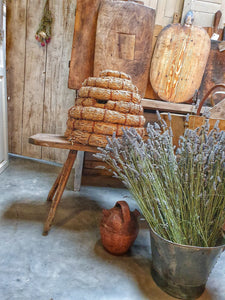 Traditional French Country Bee Skep Rustic Primitive Farmhouse sitting on antique french farmhouse bench with a bucket of cut lavender in a vintage tin rivited bucket . french farmhouse cutting boards and chopping board in the back ground. Dusty gems Interiors Nantwich 