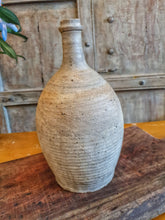 Load image into Gallery viewer, Antique Rustic Primitive French Stoneware Cider, wine or Walnut Oil Bottle sitting on painted french farmhouse table with large farmhouse chopping board this all sits infront of a pair of antique  gray painted heavy wood window shutters dusty gems interiors nantwich