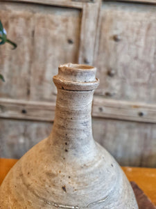 Antique Rustic Primitive French Stoneware Cider, wine or Walnut Oil Bottle sitting on painted french farmhouse table with large farmhouse chopping board this all sits infront of a pair of antique  gray painted heavy wood window shutters dusty gems interiors nantwich
