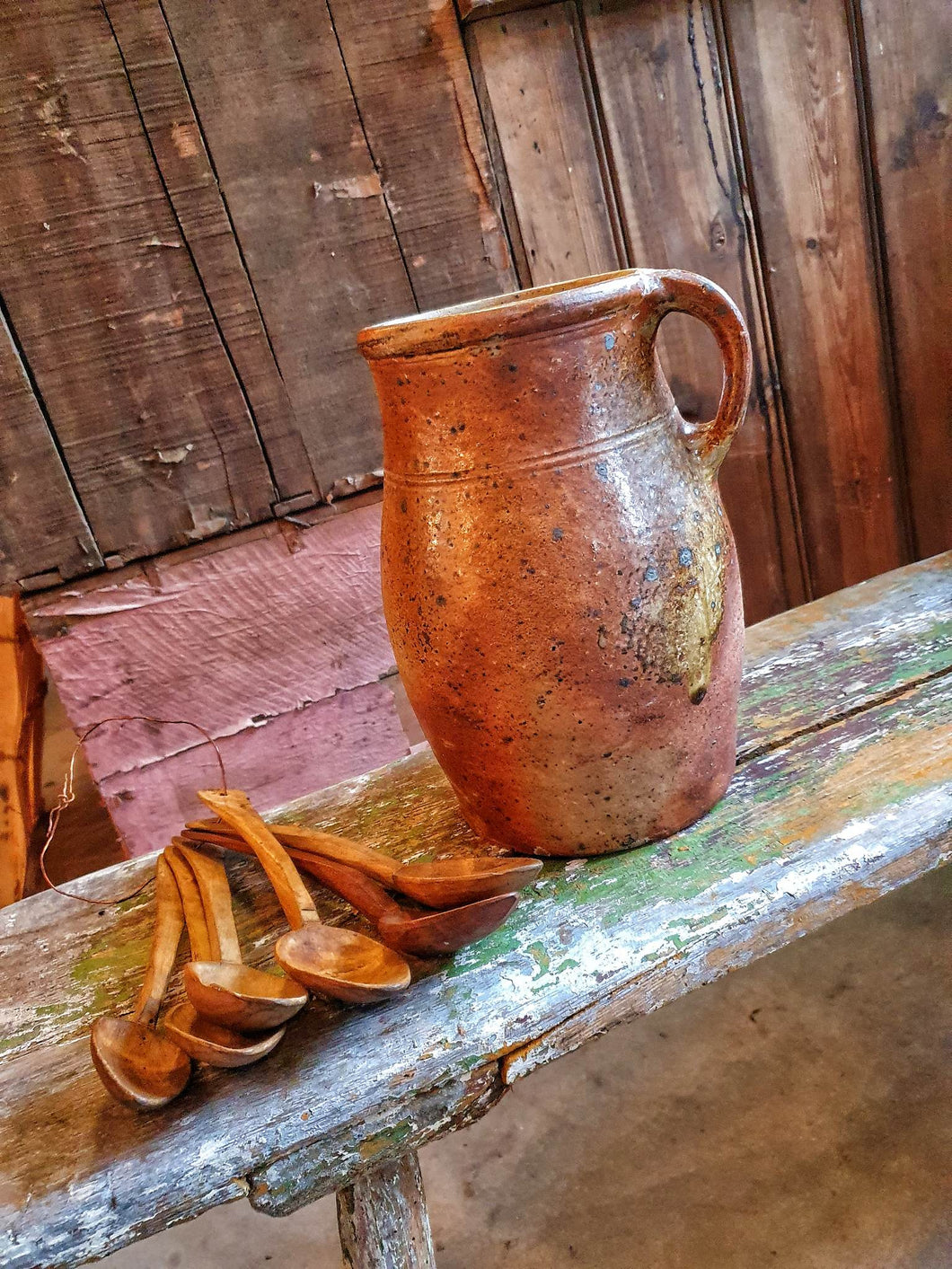Antique French Country Rustic Cider Jug 19th Century Farmhouse sitting on antique Swedish  painted farmhouse  bench with antique handcarved spoons next to the Jug  overall primitive farmhouse kitchen look Dusty Gems Interiors Nantwich 