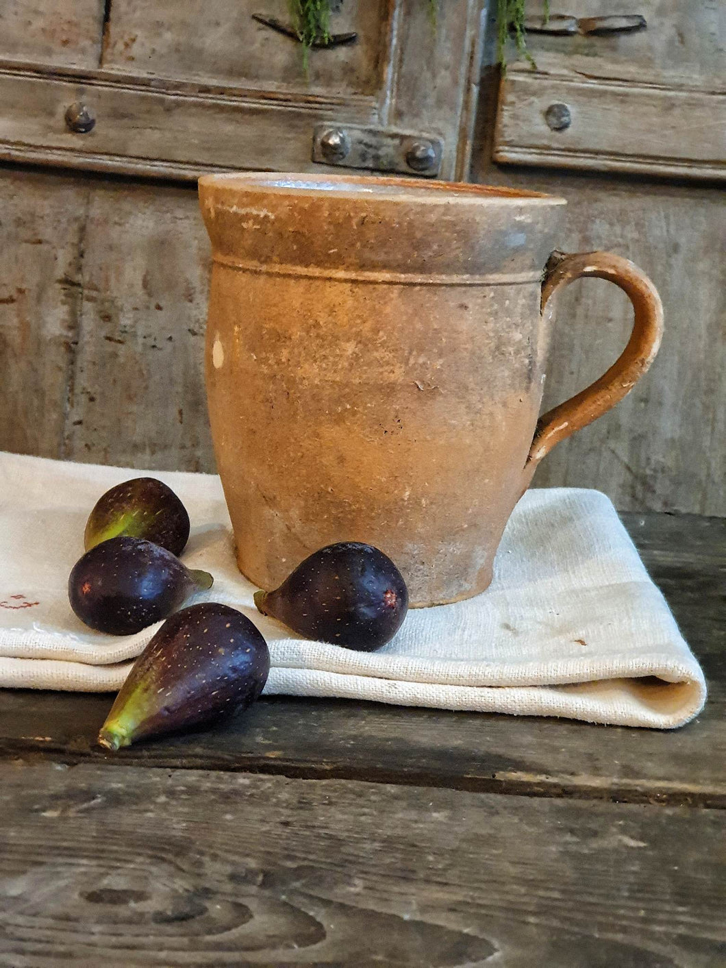 Antique French Country Rustic Terracotta Farmhouse Hand Made Jug sitting on french farmhouse table along with french 19th century linen with four fresh figs on top with a background of painted french farmhouse shutters dusty Gems interiors nantwich  